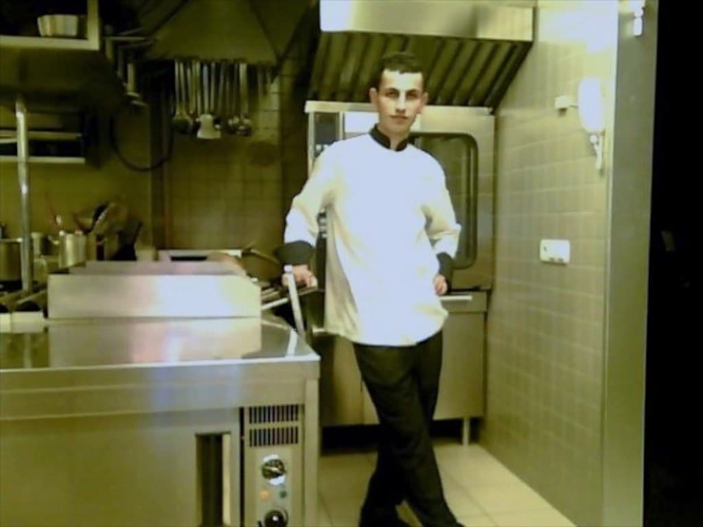 A young Sinan Camozu in chef's whites standing beside the ranges in the hotel kitchen