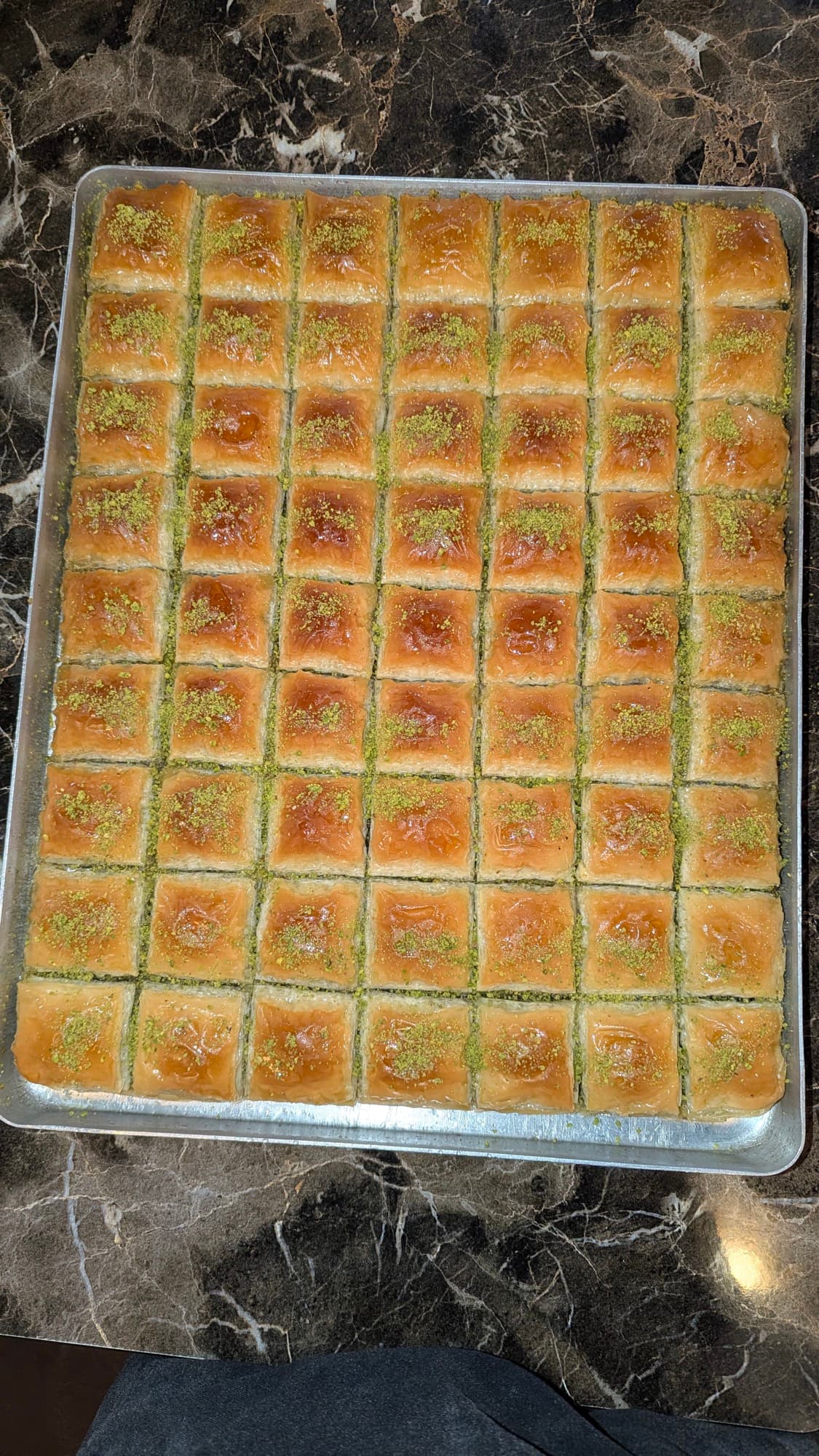 A full tray of Sultan's pistachio baklava, scored into diamonds, fresh on dark marble